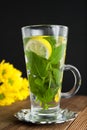 Glass Cup of mint tea ith lemon slices and yellow flowers on background. Wooden table and black background. Royalty Free Stock Photo