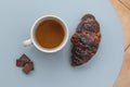 Hot cup of tea with a crispy croissant and small chocolate pieces served on a light blue table Royalty Free Stock Photo