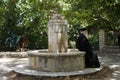 Old gray-haired priest of greek christian church meditates by the fountain