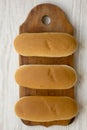 Hot dog buns on wooden board on white wooden table, top view. Flat lay, from above, overhead. Royalty Free Stock Photo