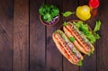 Hot dog with  sausage, cucumber, tomato and lettuce on dark wooden background. Royalty Free Stock Photo