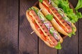 Hot dog with sausage, cucumber, tomato and lettuce on dark wooden background. Royalty Free Stock Photo