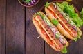 Hot dog with sausage, cucumber, tomato and lettuce on dark wooden background.