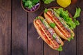 Hot dog with sausage, cucumber, tomato and lettuce on dark wooden background. Royalty Free Stock Photo