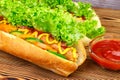 Hot dog with sausage, lettuce, tomato, cucumber, ketchup and mustard on wooden background. Royalty Free Stock Photo