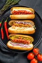 Hot dogs with assorted toppings. Delicious hot-dogs with pork and beef sausages. Black background. Top view