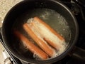 Hot dogs cooking in water in pot on stove