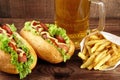 Hot dogs with glass of beer with french fries on wooden board