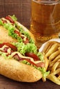 Hot dogs with glass of beer with french fries on wooden board