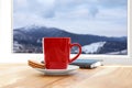 Hot drink, cookies and book near window with view of mountain landscape