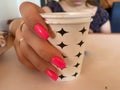 Hot drink in a craft plastic cup with a white cap in the hands of a young girl with a red manicure in a black coat close-up on the Royalty Free Stock Photo