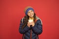 Hot drink for winter morning. Small girl hold tea cup red background. Happy child with winter look. Hot chocolate Royalty Free Stock Photo