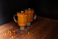 Hot drinks from sea buckthorn in two glasses on a black background. The concept of warm seasonal drinks. Sea buckthorn berries