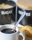 A teaspoon full of demerara sugar,being put into into a small,white cup of hot espresso coffee,in a domestic kitchen,