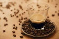 Hot espresso with foam in glass cup on vintage plate with aromatic roasted coffee beans on wooden table. Copy space. Alternative