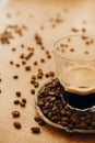 Hot espresso with foam in glass cup on vintage plate with aromatic roasted coffee beans on wooden table. Copy space. Alternative