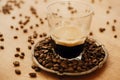 Hot espresso with foam in glass cup on vintage plate with aromatic roasted coffee beans on wooden table. Copy space. Alternative