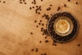 Hot espresso with foam in glass cup on vintage plate with aromatic roasted coffee beans on wooden table. Flat lay with copy space