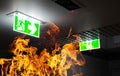 Hot flame fire and green fire escape sign hang on the ceiling in the office at night. The concept of fire escape training and prep Royalty Free Stock Photo