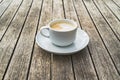 Hot foaming cappuccino in a white ceramic cup on a saucer stands on a table of wooden boards