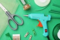 Hot glue gun and handicraft materials on green background, flat lay