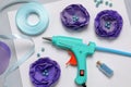 Hot glue gun, textile flowers and handicraft materials on color background, flat lay