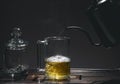 Hot tea is poured from a teapot into a glass cup, on a dark background