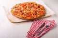 Hot homemade pizza with chicken meat, tomatoes, onions near with cutlery fork and knife on red tablecloth, angle view Royalty Free Stock Photo