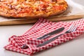 Hot homemade pizza with chicken meat, tomatoes, onions near with cutlery fork and knife on red tablecloth, angle view Royalty Free Stock Photo