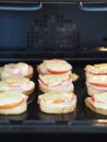 Hot homemade sandwiches with sausage, tomatoes and cheese on a baking sheet in the kitchen oven.Natural healthy food