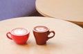 Hot latte art coffee with cocoa mocha in 2 ceramic coffee mugs on round wooden desk in modern cafe Royalty Free Stock Photo