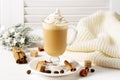 A hot latte with cinnamon and whipped cream stands on a white wooden window with shutters