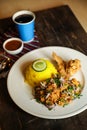 Hot Lemony Chicken Rice Meal served in plate with sauce, cold drink, spoon and fork isolated on wooden board side view of thai