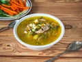 Hot lunch of spring soup with sorrel in a deep light plate and a light snack of sliced fresh carrots and fresh sorrel on a wooden Royalty Free Stock Photo