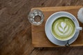 Hot Matcha Green Tea Latte in White Cup on Wood plate with some Water in Glass on Wooden table Royalty Free Stock Photo