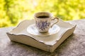 Hot morning coffee in small blue and white floral design cup on shabby chic vintage white tray on window sill in front of summer Royalty Free Stock Photo