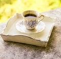 Hot morning coffee in small blue and white floral design cup on shabby chic vintage white tray on window sill in front of summer Royalty Free Stock Photo