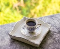 Hot morning coffee in small blue and white floral design cup on shabby chic vintage white tray on window sill in front of summer Royalty Free Stock Photo