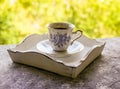 Hot morning coffee in small blue and white floral design cup on shabby chic vintage white tray on window sill in front of summer Royalty Free Stock Photo