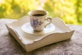 Hot morning coffee in small blue and white floral design cup on shabby chic vintage white tray on window sill in front of summer Royalty Free Stock Photo