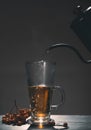 Hot mountain ash drink is poured from a teapot into a glass mug, on a dark background