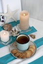 A hot mug of black tea with cookies on a striped tablecloth, wax candles, decorative starfish, seashell, pile of