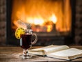 Hot mulled wine and a book on the wooden table. Fireplace with warm fire on the background