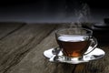 Hot organic teacup with saucer, spoon and kettle on wooden table background.