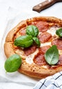 Hot pepperoni pizza with spicy salami sausage, mozzarella cheese, tomato sauce and green basil, white table background, top view