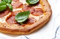 Hot pepperoni pizza with spicy salami sausage, mozzarella cheese, tomato sauce and green basil, white table background, top view