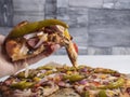 Hot pizza peppers with meat and vegetables, one piece in hand