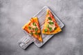 Hot pizza slices with mozzarella cheese, ham, tomato and parsley on wooden cutting board, stone concrete background