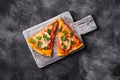 Hot pizza slices with mozzarella cheese, ham, tomato and parsley on wooden cutting board, stone concrete background