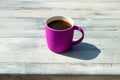 Hot purple cup of black coffee on rustic wooden bright table. Outdoor in the afternoon. Royalty Free Stock Photo